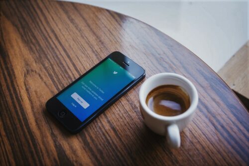 phone displaying twitter screen on desk with coffee cup